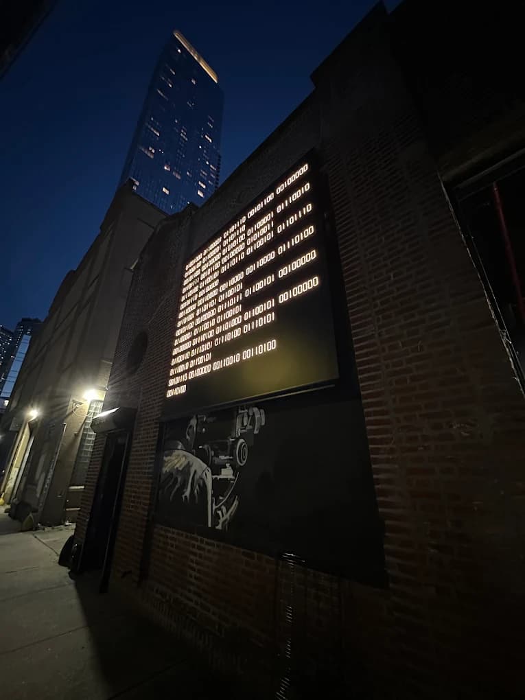 The brick facade of 00:00 in Long Island City at night, its binary-code sign lit up